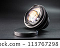 Tilted vintage camera lens on display, colorful light reflection on glass, detailed focus mechanism, photography gear against a dark background 113767298