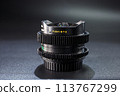 Stacked fisheye lens, engraved with FISH-EYE text, atop vintage photography equipment, dark moody background enhances professional gear appeal. 113767299