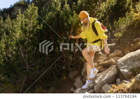 Excited woman walking through landscape outdoors. An active girl enjoys her vacation in the forested mountains. Smiling tourist on a hike. A joyful explorer going on a tourist adventure. 113768194