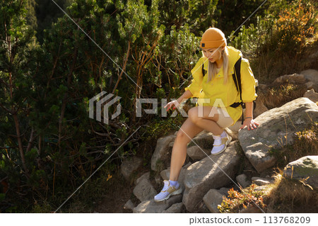 Excited woman walking through landscape outdoors. An active girl enjoys her vacation in the forested mountains. Smiling tourist on a hike. A joyful explorer going on a tourist adventure. 113768209