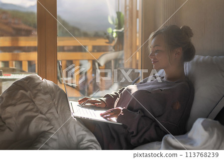 Happy casual beautiful woman working on a laptop sitting on the bed in the house. 113768239