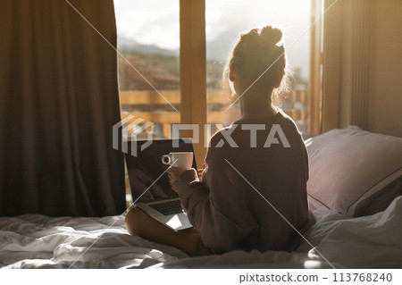 Happy casual beautiful woman working on a laptop sitting on the bed in the house. 113768240