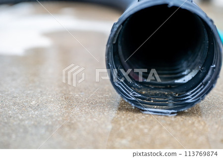 Selective focus on the front opening of a residential sump pump discharging water from the end of a flexible black hose 113769874