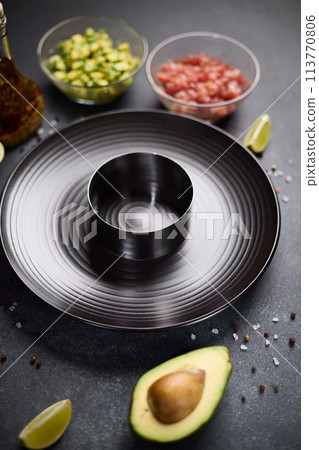 Tuna and avocado tartare recipe - sliced chopped ingredients and form on a dark table Tuna and avocado tartare recipe - sliced chopped ingredients and form on a dark table 113770806