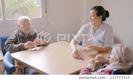 Caregiver playing cards with senior people in a geriatric 113773515