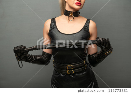 Beautiful dominant brunette mistress woman in latex dress and gloves posing with riding crop 113773881