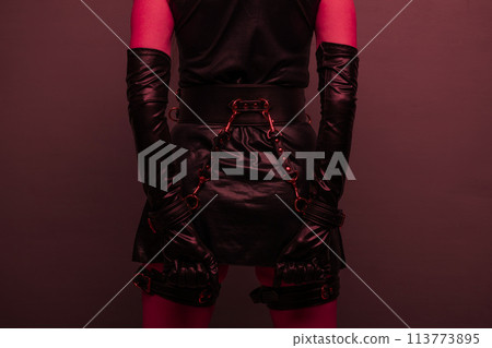 Beautiful young woman in a leather dress and bondage set posing back on red light backgound 113773895
