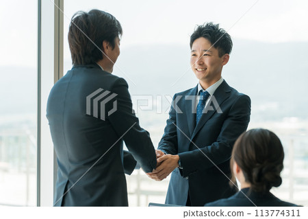 Businessmen shaking hands and signing a contract in a corporate office/conference room 113774311