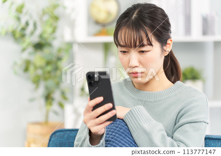 A woman looking at her smartphone with a serious expression 113777147