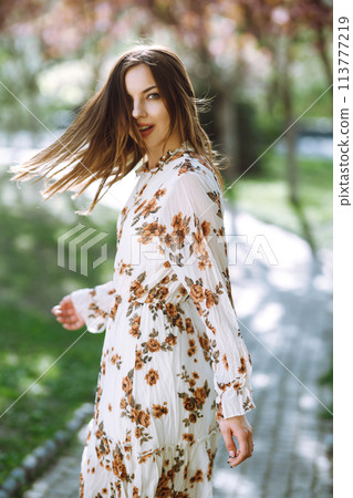 Beautiful young woman near the blooming spring tree. Attractive girl enjoying her time outside in park. Beautiful young woman near the blooming spring tree. Attractive girl enjoying her time outside in park. 113777219