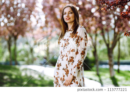 Beautiful young woman near the blooming spring tree. Attractive girl enjoying her time outside in park. Beautiful young woman near the blooming spring tree. Attractive girl enjoying her time outside in park. 113777221