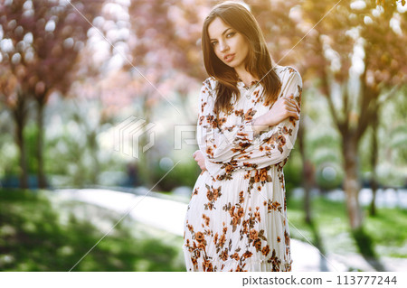 Beautiful young woman near the blooming spring tree. Attractive girl enjoying her time outside in park. 113777244