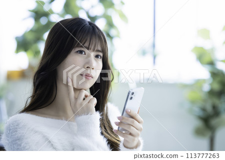 Young woman thinking while using a smartphone 113777263