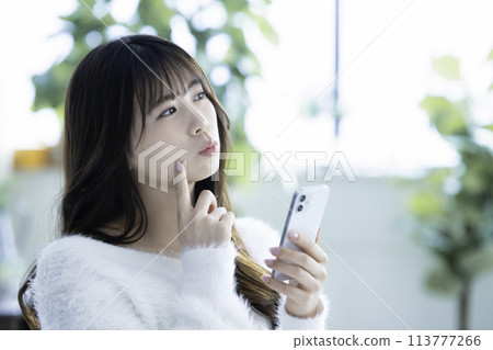 Young woman thinking while using a smartphone Young woman thinking while using a smartphone 113777266