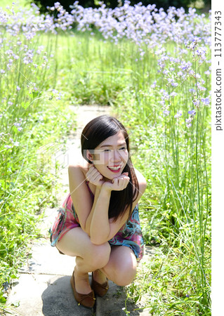 Beautiful Asian woman is smiling and relaxing in blooming purple Murdannia giganteum flowers field 113777343