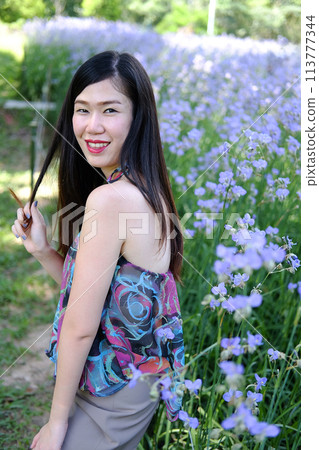 Beautiful Asian woman is smiling and relaxing in blooming purple Murdannia giganteum flowers field Beautiful Asian woman is smiling and relaxing in blooming purple Murdannia giganteum flowers field 113777344