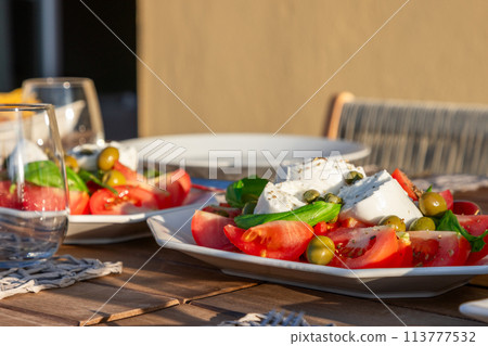 Caprese salad with Mozzarella, tomatoes, olives, and capers on a sunlit table 113777532
