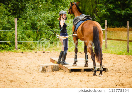 Jockey young woman getting horse ready for ride Jockey young woman getting horse ready for ride 113778394