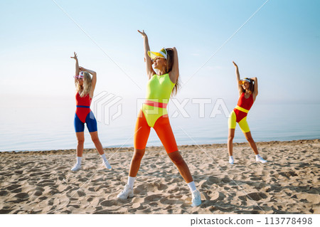 Three young woman - dancer dancing in bright swimsuits on the beach. Sport, fitness, active life. 113778498