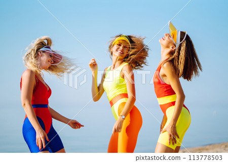 Three young woman - dancer dancing in bright swimsuits on the beach. Sport, fitness, active life. Three young woman - dancer dancing in bright swimsuits on the beach. Sport, fitness, active life. 113778503
