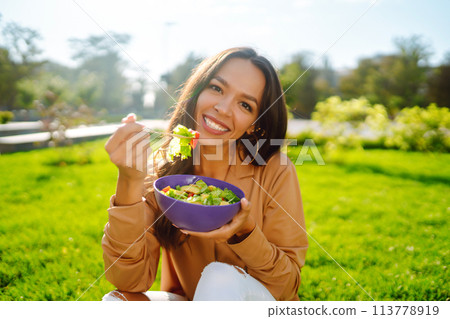 Portrait of smiling woman eating salad outdoor on sunny day. Healthy lifestyle. Concept picnic. 113778919