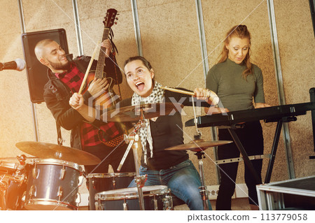Passionate emotional female drummer with her bandmates practicin 113779058
