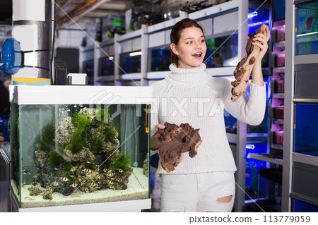 Female teenager is holding large yellow-brown sandstone for aquarium decoration 113779059