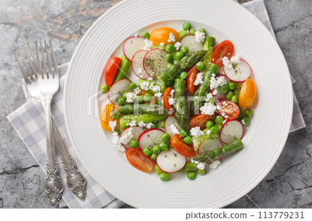 Vegetable salad of asparagus, fresh radishes, cherry tomatoes, green peas and goat cheese close-up in a plate. Horizontal top view Vegetable salad of asparagus, fresh radishes, cherry tomatoes, green peas and goat cheese close-up in a plate. Horizontal top view 113779231