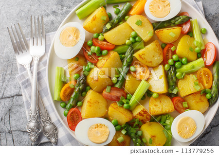 Delicious salad of potatoes, asparagus, cherry tomatoes, eggs and green peas close-up in a plate. Horizontal top view 113779256