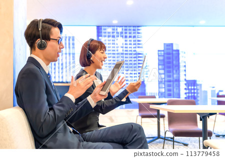 A businessman and a businesswoman wearing headsets working in a free address office 113779458