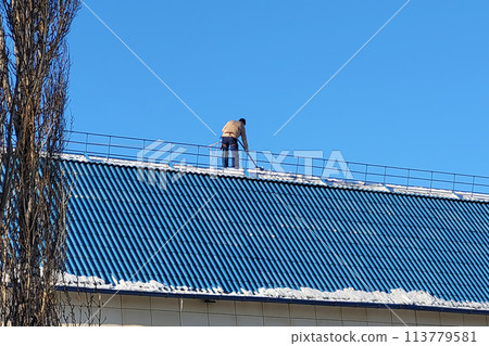 Orenburg, Russia - February 24, 2024 A worker removes snow from a city building with a shovel. Editorial 113779581