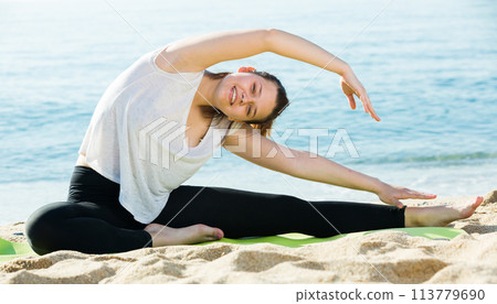Smiling adult female in white T-shirt is practicing set of stretching exercises 113779690