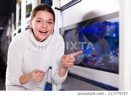 Girl near big aquarium is pointing to interesting model of aquariums Girl near big aquarium is pointing to interesting model of aquariums 113779787