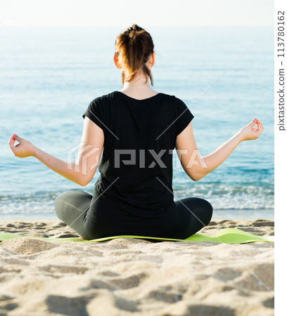 Smiling adult woman in black T-shirt is sitting her back and practicing asana Smiling adult woman in black T-shirt is sitting her back and practicing asana 113780162