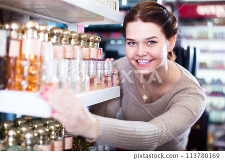cheerful woman customer deciding on perfume variants in cosmetics shop 113780169