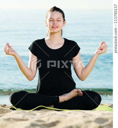 Adult female in black T-shirt is sitting and practicing asana Adult female in black T-shirt is sitting and practicing asana 113780237