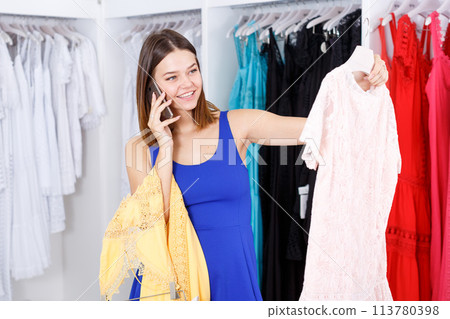 Girl choosing dress and talking on phone Girl choosing dress and talking on phone 113780398
