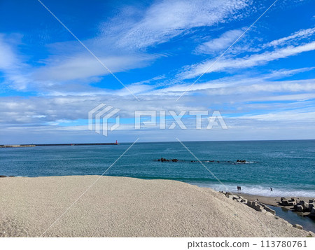 Hualien, Taiwan - 11.27.2022: Jian Stream leading to the Pacific Ocean via a beach with tetrapods and people enjoying the beach under a sunny blue sky during the pandemic with a lighthouse in sight 113780761