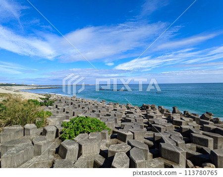 Hualien, Taiwan - 11.27.2022: A beach half-filled with tetrapod and sandy at the other side facing the Pacific Ocean with a lighthouse in sight under a sunny blue sky during the pandemic 113780765