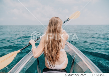 Woman in kayak back view. Happy young woman with long hair floating in transparent kayak on the crystal clear sea. Summer holiday vacation and cheerful female people relaxing having fun on the boat 113783569