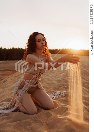 Sexy woman is kneeling in the sand, holding sand in her hands Sexy woman is kneeling in the sand, holding sand in her hands 113783976