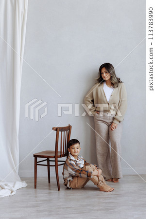 A woman and a boy are posing for a photo in a room with a wooden chair 113783990