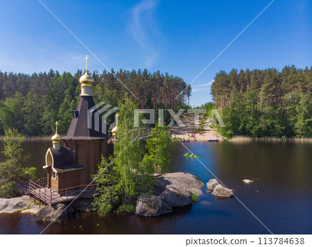 Aerial top view to wooden Church of St. Apostle Andrew First-Called on Vuoksa River with bridge. Temple on small island near village Vasilevo, Melnikovo, Priozersky District Leningrad region. Russia Aerial top view to wooden Church of St. Apostle Andrew First-Called on Vuoksa River with bridge. Temple on small island near village Vasilevo, Melnikovo, Priozersky District Leningrad region. Russia 113784638