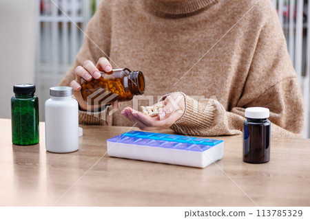 Female putting prescription pills and vitamins in a daily pill box organizer. Sorting nutritional supplements and antibiotics into weekly pills container. Female putting prescription pills and vitamins in a daily pill box organizer. Sorting nutritional supplements and antibiotics into weekly pills container. 113785329