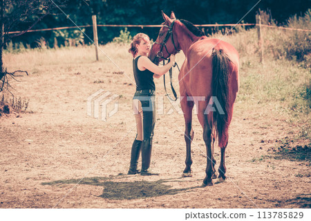 Jockey woman walking with horse on meadow Jockey woman walking with horse on meadow 113785829