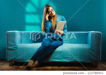 woman with tablet sitting on couch blue color 113786451