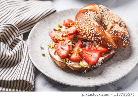 Bagel with cream cheese, strawberries and pistachio for breakfast. 113786575