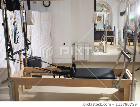 Woman training pilates on the reformer bed. Reformer pilates studio machine for fitness workouts in gym. Fit, healthy and strong authentical body. Fitness concept 113786759
