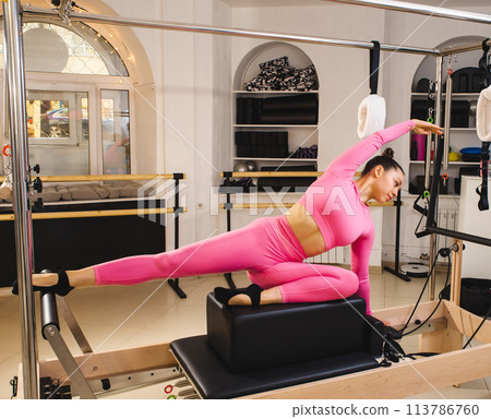 Two beautiful fit-shape females dressed sporty doing ABS muscles strength exercises using pilates reformer machine in sport athletic gym. Active people training or medical rehabilitation concept image 113786760