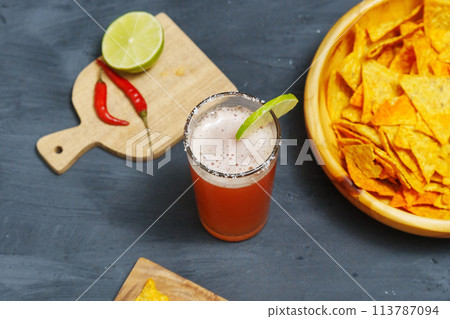 Michelada cocktail with tomato juice, beer and lime in a glass and nachos. Selective focus Michelada cocktail with tomato juice, beer and lime in a glass and nachos. Selective focus 113787094